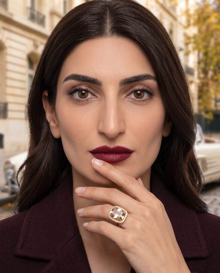 Luxury jewellery editorial portrait featuring a woman wearing a statement ring and burgundy lipstick in a classic urban setting.