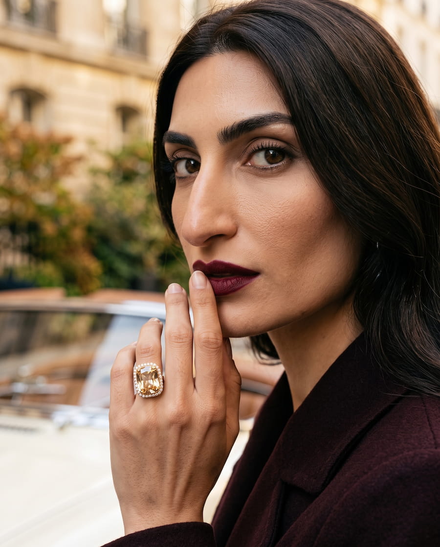 Close-up fashion portrait showcasing a gold statement ring with a large central stone and decorative detailing.