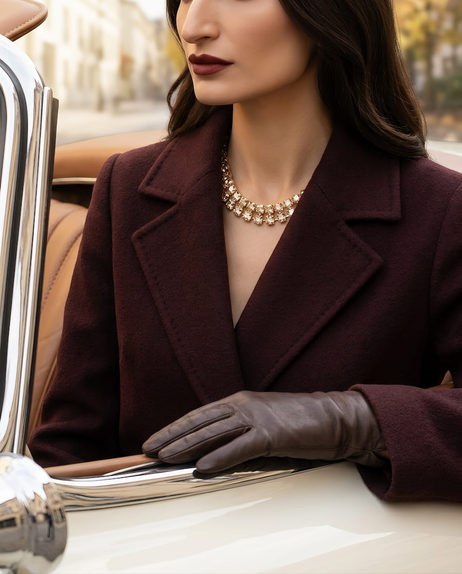Close-up editorial photograph featuring a gold statement necklace, burgundy coat, and leather gloves beside a classic cream-coloured car, showcasing the VOA luxury jewellery concept.